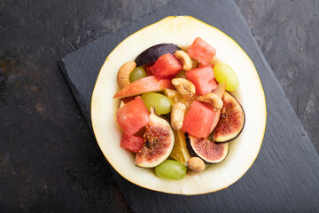 Vegetarian fruit salad of watermelon, grapes, figs, pear, orange, cashew  on black concrete...