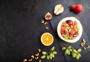 Vegetarian fruit salad of watermelon, grapes, figs, pear, orange, cashew on black concrete background. Top view, copy space.