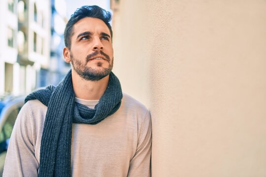 Young hispanic man smiling happy wearing scarf leaning on the wall at the city.