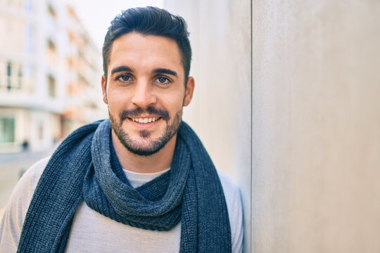 Young hispanic man smiling happy wearing scarf leaning on the wall at the city