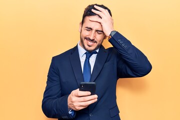 Young hispanic man wearing suit using smartphone stressed and frustrated with hand on head, surprised and angry face