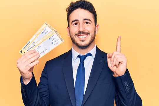 Young hispanic man wearing suit holding boarding pass smiling happy pointing with hand and finger to the side