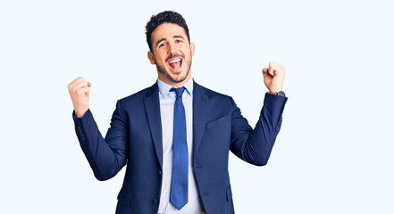 Young hispanic man wearing business clothes screaming proud, celebrating victory and success very excited with raised arms