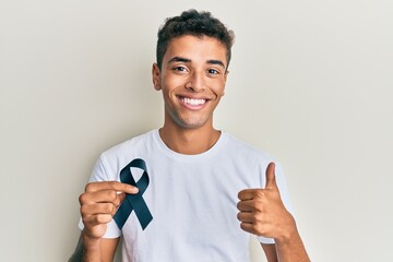 Young handsome african american man holding black ribbon smiling happy and positive, thumb up doing excellent and approval sign