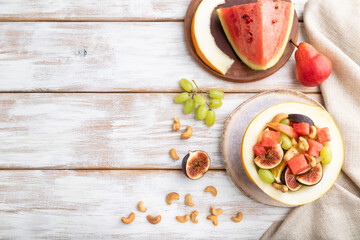 Vegetarian fruit salad of watermelon, grapes, figs, pear, orange, cashew on white wooden background. Top view, copy space.