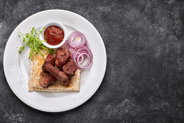 shashlik, with sauce, onions, and lavash, on a white plate, on a dark background