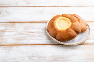 Sour cream bun on a white wooden background. Side view, copy space.