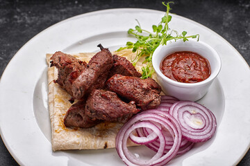 shashlik, with sauce, onions, and lavash, on a white plate, on a dark background