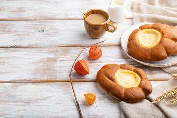 Sour cream bun with cup of coffee on a white wooden background. Side view, copy space.