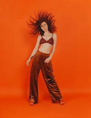Redhead curly girl in the studio on an orange background in stylish clothes
