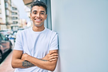 Obraz premium Young latin man smiling happy leaning on the wall at the city.