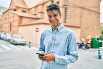 Young latin man smiling happy using smartphone walking at the city.