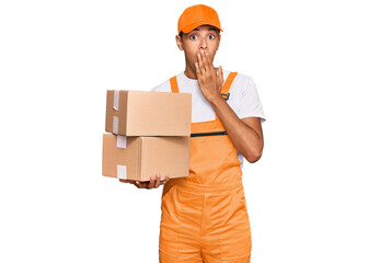 Young handsome african american man holding delivery package covering mouth with hand, shocked and...