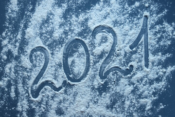 The inscription 2021 on a dark surface covered with flour. Written numbers 2021 with your finger on flour. Christmas or new year concept.