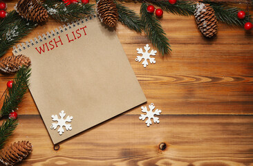 The inscription wish list in a notebook on a wooden background next to the branches of a Christmas tree with cones and red berries. The view from the top.