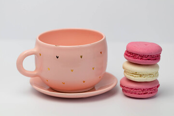 Macaroons next to a pink cup. Isolated over white background. Homemade colorful macaroons in French style.