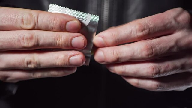 Man is opening condom. Close-up view on hands.
