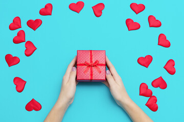 Woman hands holding red gift box on blue background with many hearts, copyspace. Happy Valentine Day background