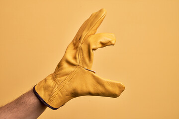 Hand of caucasian young man with gardener glove over isolated yellow background picking and taking...