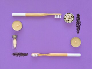 Bamboo toothbrushes, toothpaste in tablets, dental floss, candles and dried flowers. Rectangular frame on a violet background. Ecology, zero waste.