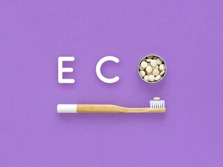 Bamboo toothbrush and toothpaste in tablets. Word Eco on a violet background. Plastic free, zero waste.