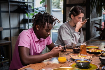 Cropped shot of a group of friends having a breakfast in the common kitchen. Gadget addiction concept.