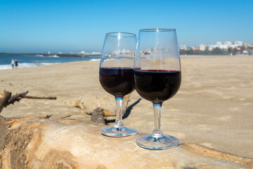 Tasting of different fortified dessert ruby, tawny port wines in glasses on sandy beach with view on waves of Atlantic ocean near Vila Nova de Gaia and city of Porto, Portugal