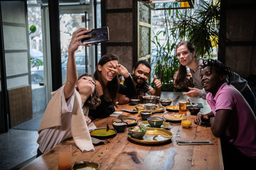 A multicaltural group of students taking photos of themselves, making crazy faces. In a cafe.
