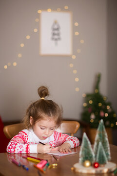 child writes letter to Santa Claus at home. little girl draws with crayons on background of Christmas devoration. concept of new year kids creativity