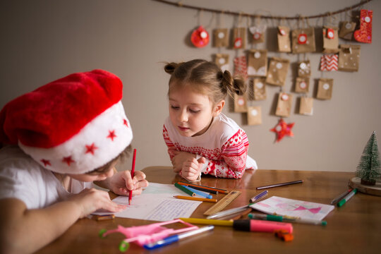 children write letter to Santa Claus at home. sisters girls draw on background of Christmas devoration. concept of new year kids preparation and anticipation.