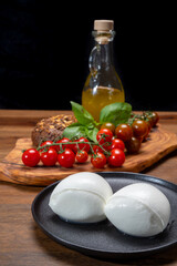 Cheese collection, white balls of soft Italian cheese mozzarella, served with red cherry tomatoes, fresh basil leaves