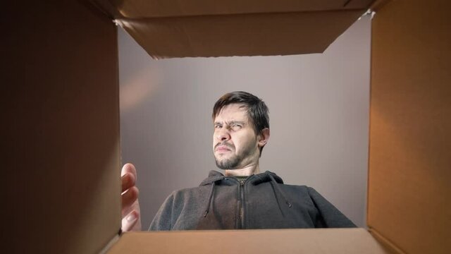 Young sad and disappointed man is opening gift and looking inside cardboard box.