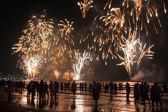 Several people at a New Year celebration in the city with fireworks on the beach. Silhouettes and reflection in the water.