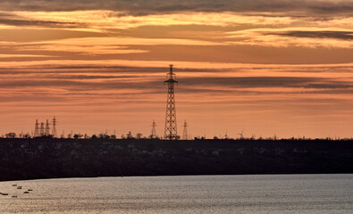 Power lines on an island in the sea against the backdrop of a yellow-orange multicolored sunset