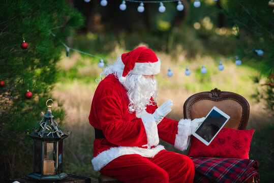 Santa Claus working holding in hands tablet pc computer with blank space, festive background. Time for buying gift, equipment, service using internet shop or sending message. Close up image.