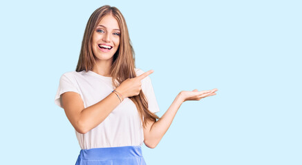 Young beautiful blonde woman wearing summer style amazed and smiling to the camera while presenting with hand and pointing with finger.