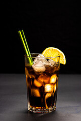 long island ice tee cocktail in a transparent glass on a black background with eco-friendly paper tubes and decorated with a slice of lemon. vertical image. close-up. frontal shooting