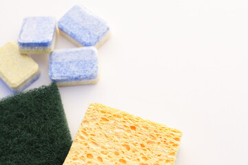 Kitchen sponges and wash machine tablets, yellow and green kitchenware and soap on white, close up isolated domestic wash tool
