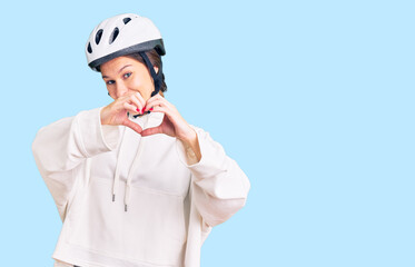Beautiful brunette young woman wearing bike helmet and sporty clothes smiling in love doing heart symbol shape with hands. romantic concept.