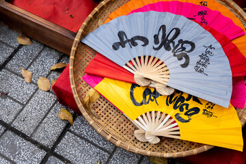 Colorful New Chinese year hand fan with peace and good luck messages, lying on a basket, in Vietnam