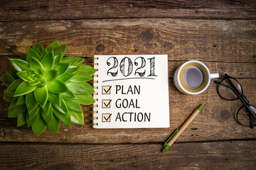 New year goals 2021 on desk. 2021 resolutions list with notebook, coffee cup and eyeglasses on...