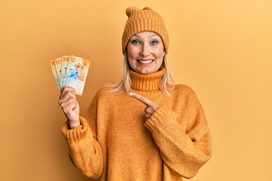 Middle age caucasian woman holding swiss franc banknotes smiling happy pointing with hand and finger