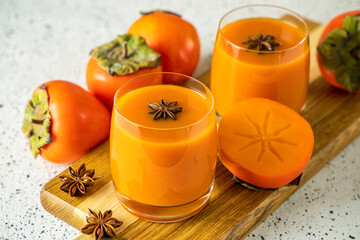 Two glasses of fresh healthy persimmon smoothie with anise stars on cutting wooden board, gray...