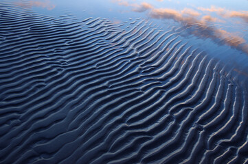 Blue sand ripples with dusk clouds reflected in water