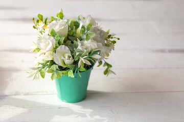 White-green artificial flowers in agreen metal bucket on white wooden table. Copy space. Shallow depth of field