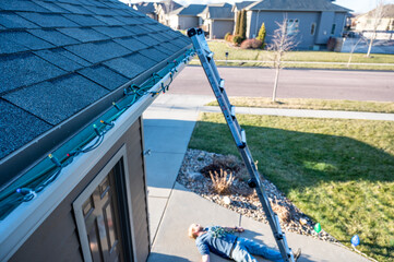 Subjective focus on Christmas lights on gutter.  Blurred background of a ladder and fallen adult on the concrete