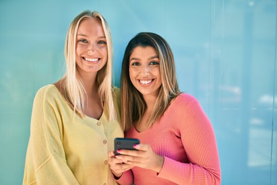 Two beautiful and young girl friends together having fun at the city using smartphone