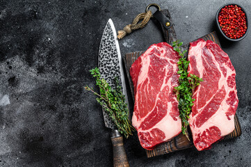 Raw chuck eye roll steaks premium beef meat on a cutting board. Black background. Top view. Copy...