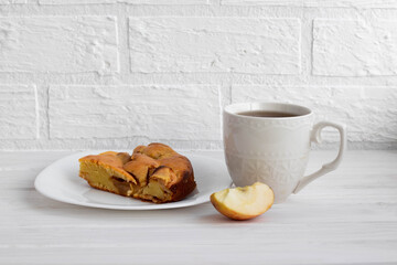 a white Cup with tea next to a piece of delicious ruddy Apple pie on a white plate