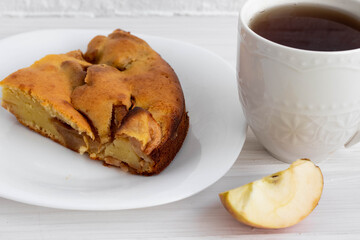 a white Cup with tea next to a piece of delicious ruddy Apple pie on a white plate